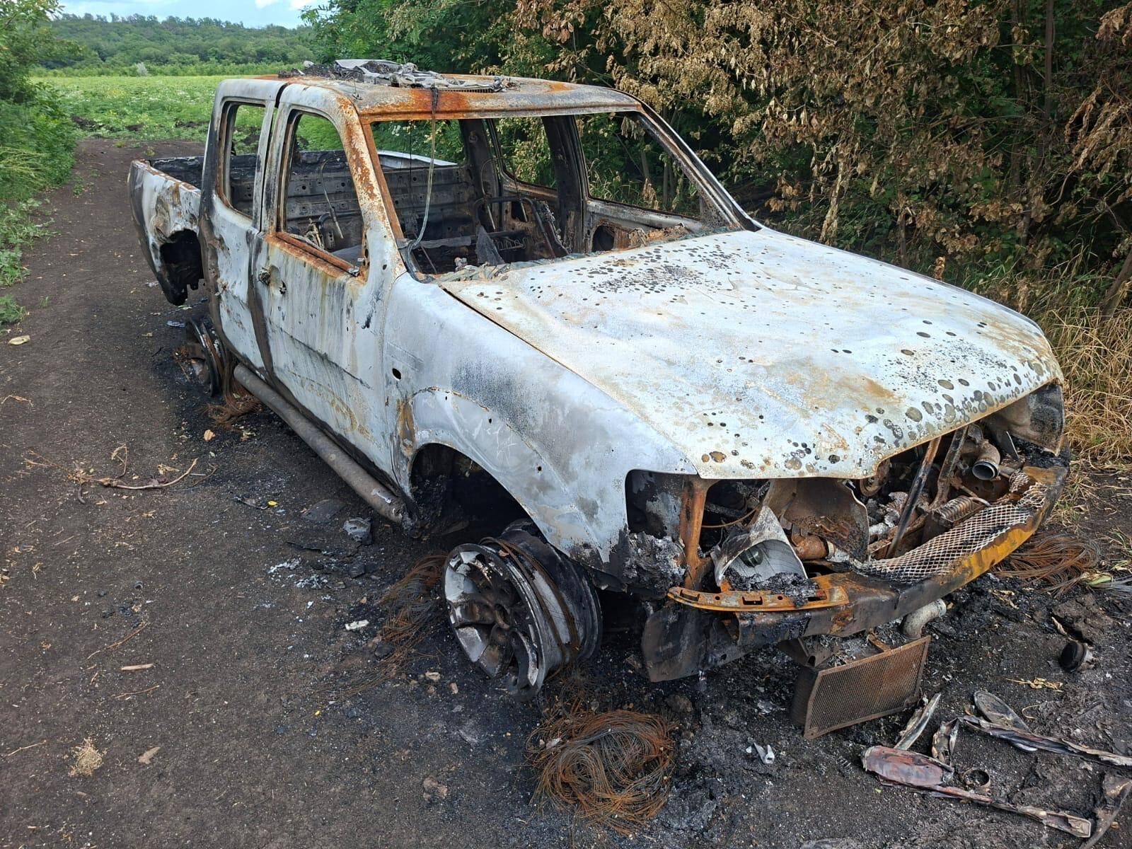 Vypálený pickup po zásahu ruským dronom, prestrelená kapota, zvyšky drôtov v tráve